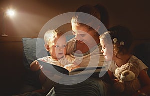 Happy family mother and children read a book in bed