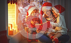 Family mother and children read a book at christmas near firep