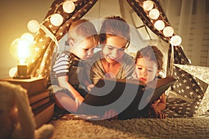 Happy family mother and children reading a book in tent at hom