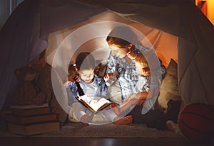 Happy family mother and children reading a book in tent at hom