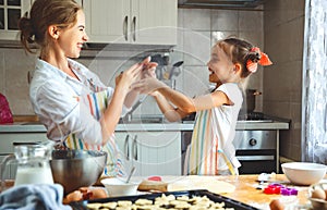 Happy family mother and daughter bake kneading dough in kitchen