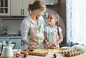 Happy family mother and daughter bake kneading dough in kitchen