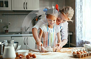 Happy family mother and daughter bake kneading dough in kitchen photo