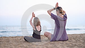 Happy family mother and daughter do yoga, meditate in lotus position on beach