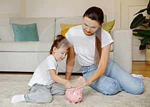 Happy Family Mother And Daughter Putting Coins In Piggy Bank At Home