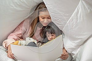 Happy family mother and daughter read a book on bed in bedroom, Asian family loving concept