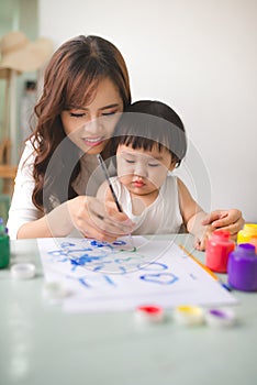 Happy family mother and daughter together paint. Asian woman helps her child girl.