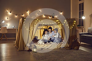 Happy family mother with daughters kid reading book sitting in tent at home