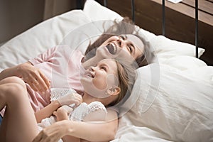 Happy family mother embracing kid daughter laughing lying on bed