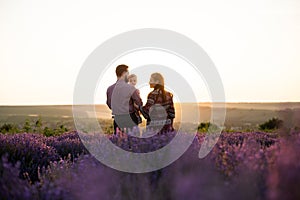 Happy family mother father and baby daughter standing on a lavender field. Mom dad and a little child hugging on a field in the mo