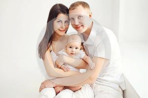 Happy family mother and father with baby at home in white room