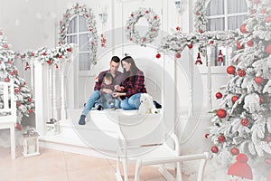 Happy family mother father baby sitting on porch of christmas de