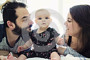 Happy family, mother, father and baby on the white bed