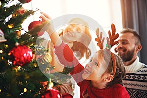 Happy family mother, father and child daughter decorate Christmas tree