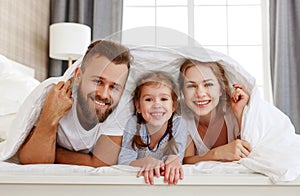 Happy family mother, father and child  laughing, playing and smiling in bed   at home