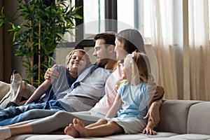 Happy family, mother, father and children hugging, relaxing on couch