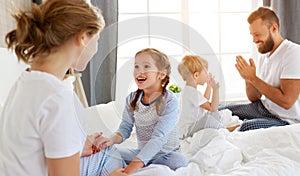 Happy family mother, father and children laughing, playing, fights pillows and jumping in bed   at home