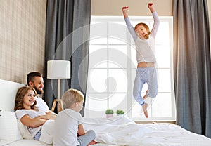 Happy family mother, father and children laughing, playing, fights pillows and jumping in bed   at home