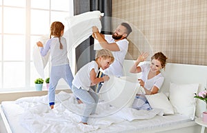 Happy family mother, father and children laughing, playing, fights pillows and jumping in bed   at home