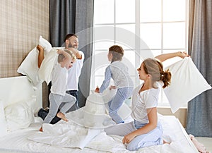 Happy family mother, father and children laughing, playing, fights pillows and jumping in bed   at home