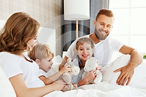 Happy family mother, father and children laughing, playing and hugging in bed   at home