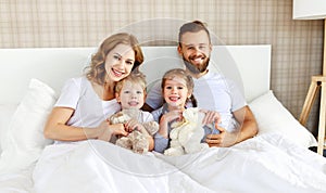 Happy family mother, father and children laughing, playing and huging in bed   at home