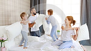 Happy family mother, father and children laughing, playing and jumping in bed   at home