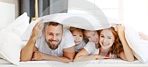 Happy family mother, father and children laughing, playing and smiling in bed   at home