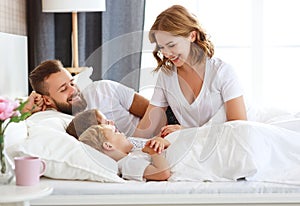Happy family mother, father and children laughing, playing and smiling in bed   at home