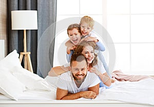 Happy family mother, father and children laughing, playing and smiling in bed   at home