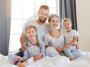 Happy family mother, father and children laughing, playing and smiling in bed   at home