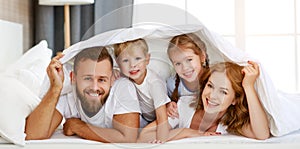 Happy family mother, father and children laughing, playing and smiling in bed   at home