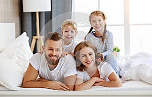 Happy family mother, father and children laughing, playing and smiling in bed   at home