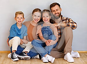 Happy family mother father and children sitting on floor against empty grey wall