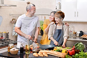 Happy family of mother father and daughter cooking in kitchen making healthy food together feeling fun