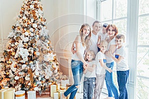 Happy family mother father five children relax playing near Christmas tree on Christmas eve at home. Mom dad daughter