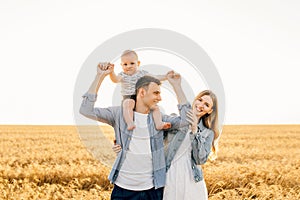 Happy family, mother, father and little child on the ripe wheat field