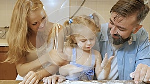 Happy family mother, father and little daughter in the kitchen preparing pies from the test.