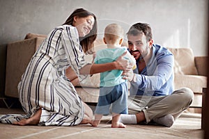Happy family - mother and father playing with a baby at home