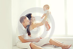 Happy family, mother and father playing with little baby home in white room near window