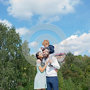 Happy family - mother, father and son on sky background in summer. Daddy mom and child son. Child sits on the shoulders