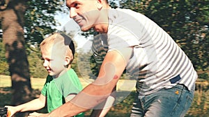 Happy family, mother, father and son are walking by nature, the child is riding a bicycle, his parents help him to