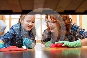 Happy family mother and kid daughter clean room at home. Middle-aged woman and little child girl wiped floor under bed