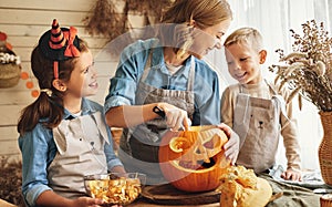 Happy family mother and kids carving pumpkin for Halloween holiday together at home