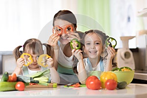 Happy family mother and kids having fun with food vegetables at kitchen holds pepper before their eyes like in glasses