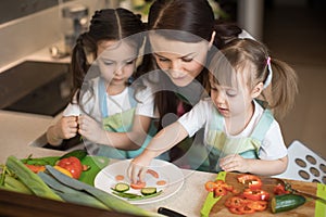 Happy family mother and kids are preparing healthy food, they make funny face with vegetables morsel in the kitchen