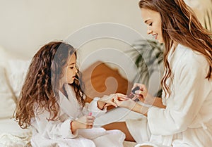 Happy family mother and little daughter in bathrobe makes manicure, laugh  on Spa day at home