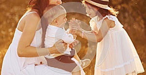 Happy family of mother, little son and daughter spending free time on the field at sunny day time of summer