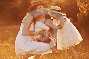 Happy family of mother, little son and daughter spending free time on the field at sunny day time of summer