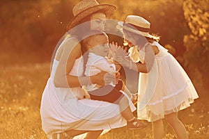 Happy family of mother, little son and daughter spending free time on the field at sunny day time of summer